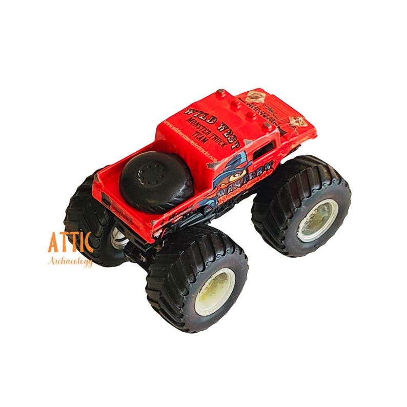 Pode incluir: Brinquedo de caminh&atilde;o monstro vermelho com a inscri&ccedil;&atilde;o "Wild West Monster Truck Team" no lado. O caminh&atilde;o tem um pneu sobressalente na parte traseira e grandes rodas pretas.
