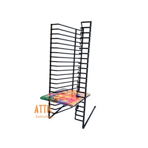 May include: A black metal wire rack designed for storage with multiple horizontal slots. A single rectangular item with a colorful graphic cover featuring the word BRASILEIRO is placed on the bottom shelf of the rack. The rack has a tall, open frame.