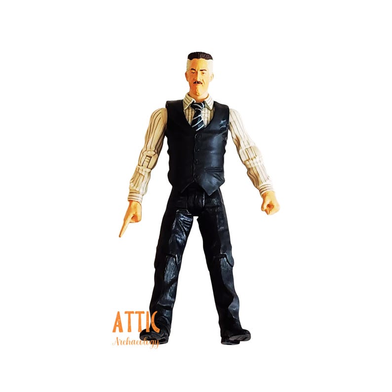 May include: A figurine of a man in a black vest, black pants, and a striped shirt. The figure has a mustache and is pointing with one hand. The figure is standing on a white surface.