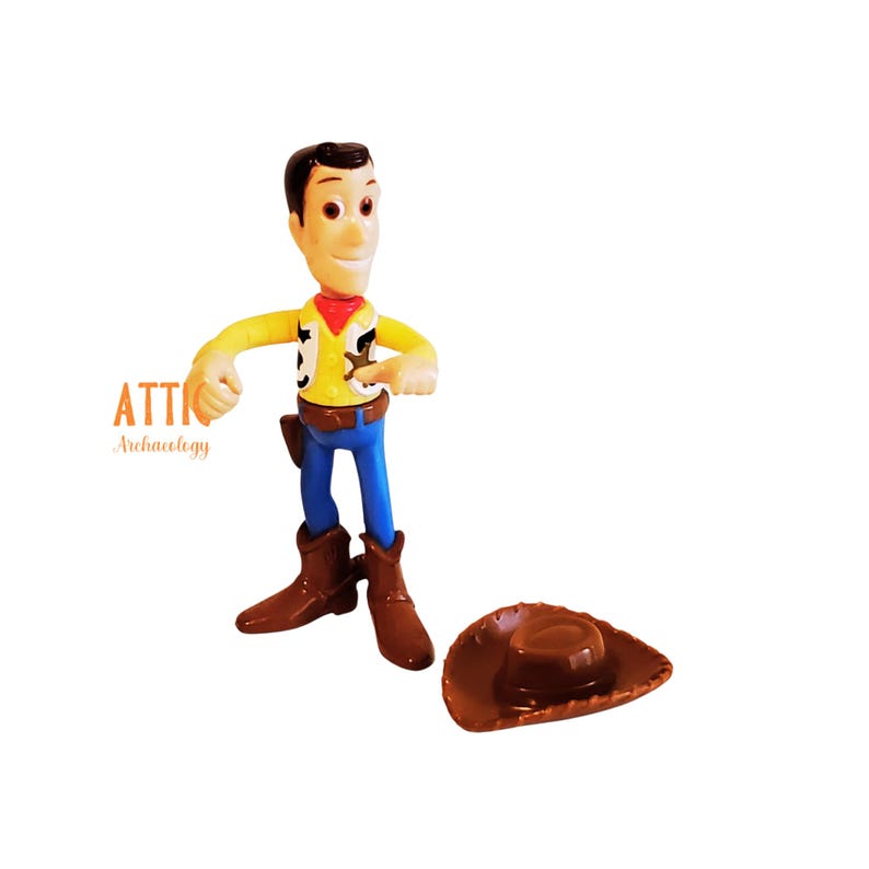 May include: A Woody action figure from the Toy Story franchise. The figure is wearing a yellow shirt, blue pants, brown boots, and a brown cowboy hat. The figure has a red neckerchief and a sheriff's badge.