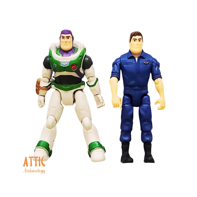 Peut inclure: Deux figurines du film Toy Story. L'une est Buzz l'&Eacute;clair dans une combinaison spatiale blanche, verte et violette. L'autre est un homme en uniforme bleu. Les figurines sont sur fond blanc. Le logo Attic Archaeology est visible.