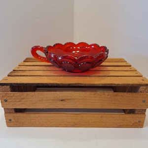 May include: A red glass bowl with a scalloped edge and a handle. The bowl has a textured surface with small circles.