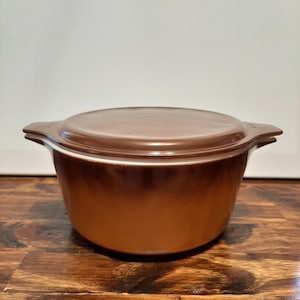 May include: A brown ceramic casserole dish with a white rim and a matching lid. The dish has a glossy finish.