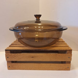 May include: A brown glass casserole dish with a lid. The dish is sitting on a wooden crate.