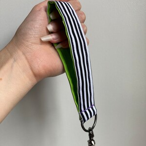 Puede incluir: Un cord&oacute;n rayado en blanco y negro con un respaldo verde y un cierre giratorio plateado.