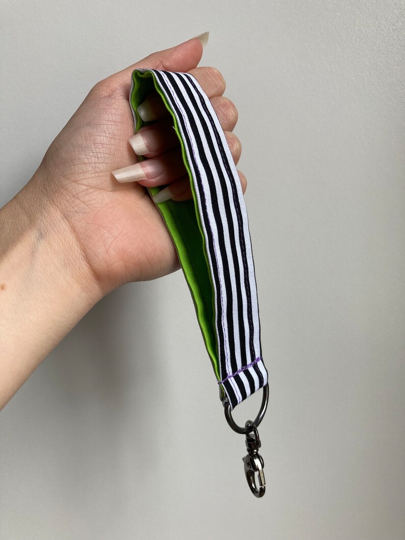 Puede incluir: Un cord&oacute;n rayado en blanco y negro con un respaldo verde y un cierre giratorio plateado.