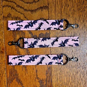 May include: Three pink keychains with black bats printed on them. Each keychain has a silver metal ring and a silver metal clasp.