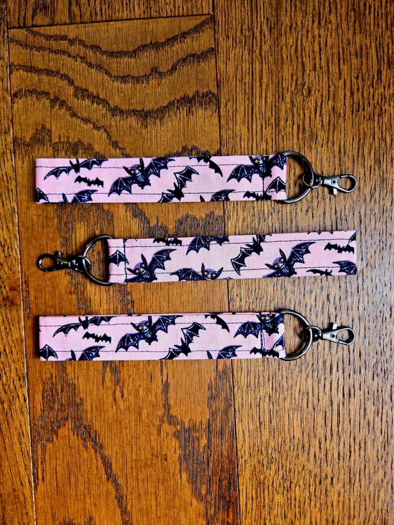 May include: Three pink keychains with black bats printed on them. Each keychain has a silver metal ring and a silver metal clasp.