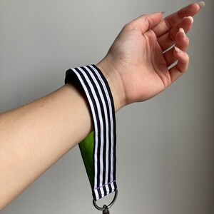 Puede incluir: Llavero a rayas blanco y negro con respaldo verde y clip plateado.