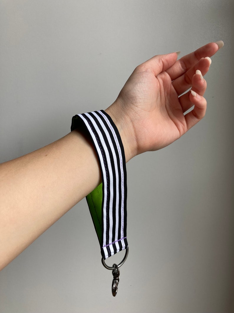 Puede incluir: Llavero a rayas blanco y negro con respaldo verde y clip plateado.