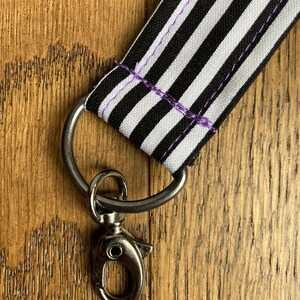 Puede incluir: Lanyard de tela a rayas blancas y negras con un cierre giratorio plateado.