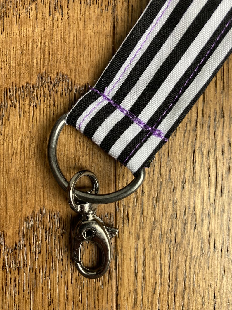 Puede incluir: Lanyard de tela a rayas blancas y negras con un cierre giratorio plateado.
