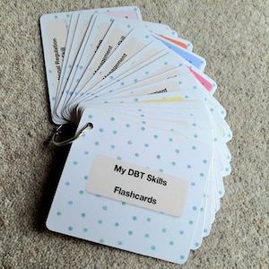 May include: A set of white DBT Skills flashcards with blue polka dots. The cards are bound together with a silver ring. The front cover of the cards reads "My DBT Skills Flashcards".