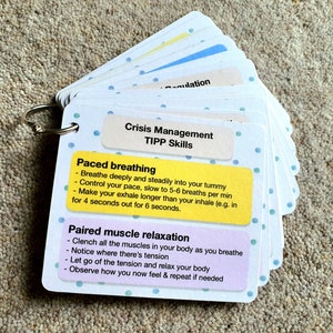 May include: A set of white cards with blue polka dots, held together with a silver ring. The cards have yellow and purple sections with text that reads "Crisis Management TIPP Skills", "Paced breathing", "Breathe deeply and steadily into your tummy", "Control your pace, slow to 5-6 breaths per min", "Make your exhale longer than your inhale (e.g. in for 4 seconds out for 6 seconds.", "Paired muscle relaxation", "Clench all the muscles in your body as you breathe", "Notice where there's tension", "Let go of the tension and relax your body", "Observe how you now feel & repeat if needed".