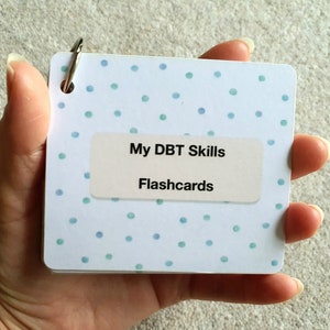 May include: A white and blue polka dot DBT Skills Flashcards booklet with a silver ring binder.