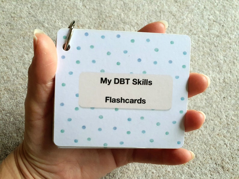May include: A white and blue polka dot DBT Skills Flashcards booklet with a silver ring binder.