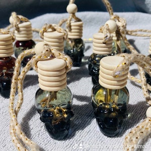 May include: A collection of small glass bottles shaped like skulls, filled with colorful liquid and topped with wooden lids. Each bottle is attached to a string with a wooden bead at the end. The bottles are arranged on a white surface.