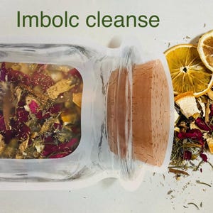 May include: A flat pouch shaped like a glass jar with a cork stopper, containing a blend of dried herbs, flower petals, and citrus pieces. The text Imbolc cleanse is printed above the pouch, with loose dried ingredients scattered to the right.