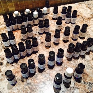 May include: A collection of small, blue glass bottles with black caps and white labels. The bottles are arranged in a semi-circle on a light brown surface.
