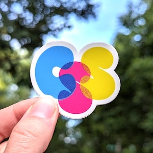 Puede incluir: Una pegatina con las letras "CS" en un diseño colorido y superpuesto. Las letras son azules, amarillas y rosas.