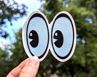 May include: A pair of googly eyes with black pupils and white highlights, printed on a white sticker with a blue background.