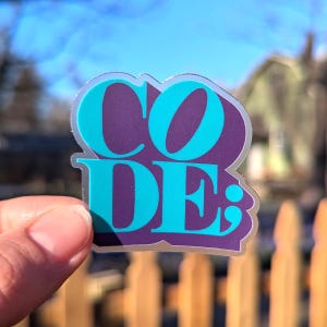 May include: A clear sticker with the word "CODE;" in turquoise letters on a purple background.