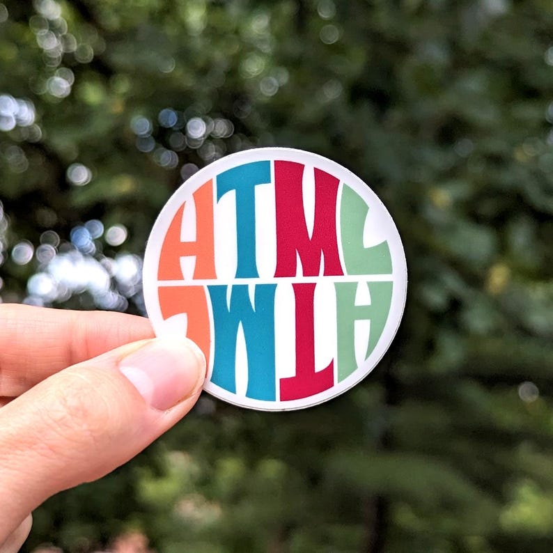 An image of an HTML sticker that's in retro 70's style lettering, against a natural outdoor background