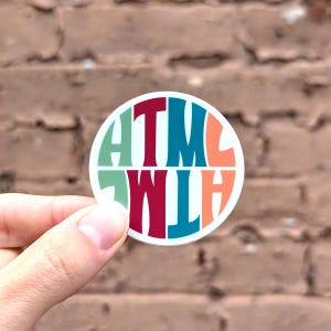 May include: A round sticker with the letters "ATWLH" in a circle, with each letter in a different color: green, red, teal, orange, and red.