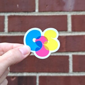 K&ouml;nnte beinhalten: Ein Aufkleber mit den Buchstaben "CS" in einem farbenfrohen, &uuml;berlappenden Design. Das "C" ist blau, das "S" ist gelb und die &Uuml;berlappung ist pink.