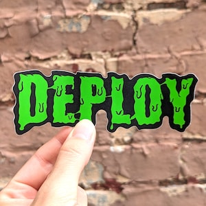 Może przedstawiać: Czarna naklejka z napisem "DEPLOY" w spływających neonowych zielonych literach. Naklejka jest trzymana na tle zwietrzałej ceglanej ściany.
