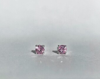 May include: A pair of stud earrings featuring square-cut, light pink gemstones set in silver-colored metal. The earrings are displayed against a white background, highlighting their color and design. These earrings are a classic jewelry item.