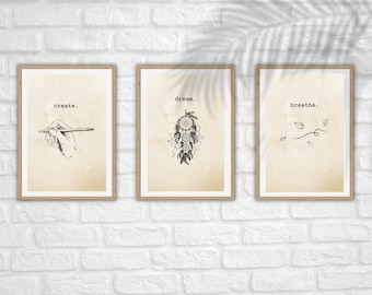 May include: Three framed wall art prints with a light beige background. The first print shows a hand holding a pencil with the text create. The second print features a dreamcatcher illustration with the text dream. The third print displays leaves with the text breathe.