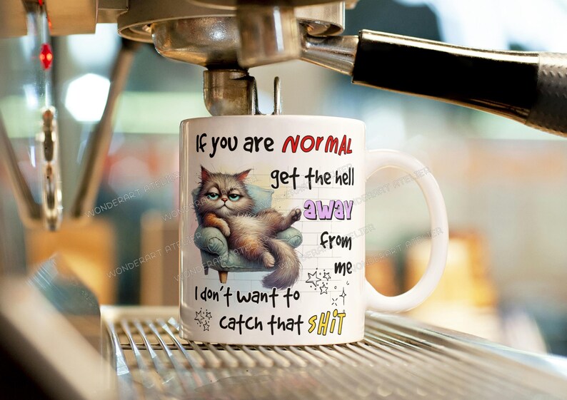 May include: White ceramic mug with a humorous cat illustration and text. The cat is lounging on a small armchair. The mug has the text "If you are NORMAL get the hell away from me I don't want to catch that SHIT."