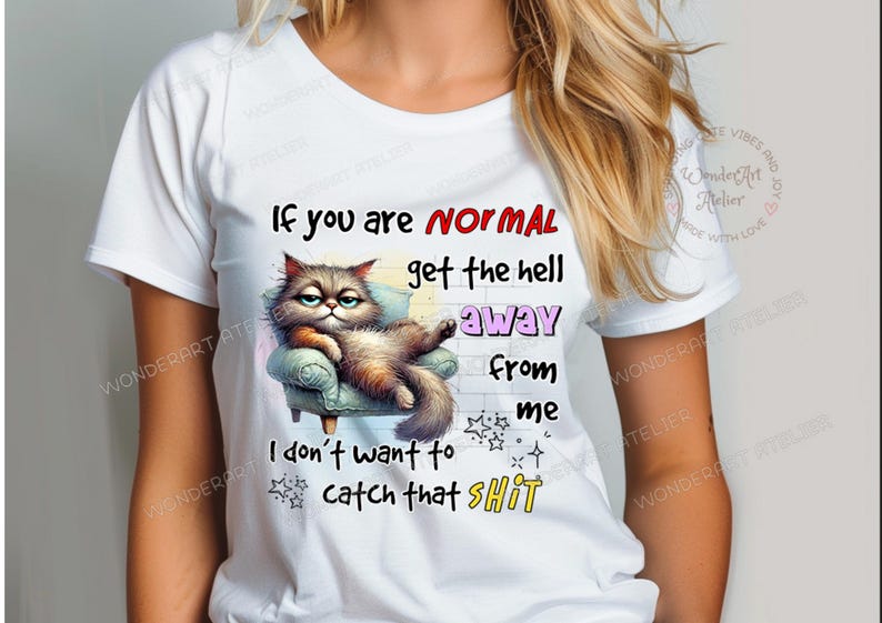 May include: White t-shirt featuring a grumpy cat illustration lounging on a small armchair. The shirt has the text "If you are NORMAL get the hell away from me I don't want to catch that SHIT".