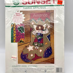 May include: A Sunset Fabric Applique kit for a Country Angel Stocking. The kit includes fabric, thread, and instructions. The finished stocking is 40cm long. The design features an angel with the word "Rejoice!" and the name "Amanda".