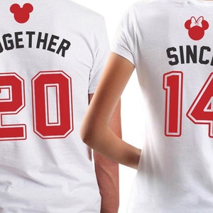 May include: Two white t-shirts with red numbers and black text. The first shirt says "TOGETHER 20" and the second shirt says "SINCE 14". Both shirts have a red Mickey Mouse head with black ears.