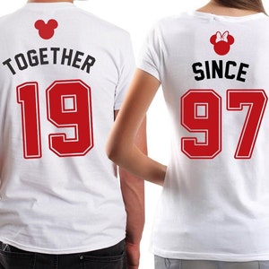 Puede incluir: Dos camisetas blancas con texto rojo y una silueta de Mickey Mouse. La camiseta de la izquierda dice "Together 19" y la camiseta de la derecha dice "Since 97".