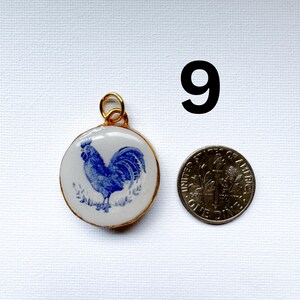 May include: A round pendant featuring a blue and white rooster illustration, encased in a gold-toned metal frame with a jump ring. The pendant is positioned next to a United States dime for scale, with the number 9 printed in black above.