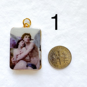 May include: Rectangular pendant with a gold-colored bail featuring a classical painting of two figures embracing. The pendant is next to a U.S. dime for size comparison. The painting has a gold border.
