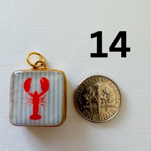 May include: A square pendant featuring a red lobster graphic on a light blue and white striped background, framed in gold with a jump ring at the top. The pendant is shown next to a United States one dime coin for scale, with the number 14 above.