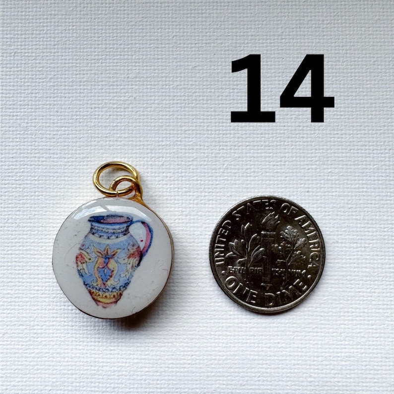 May include: A round pendant featuring a painted blue and yellow pitcher design with a gold-toned metal bail, positioned next to a United States one dime coin for scale. The number 14 is printed in large black text in the upper right corner.