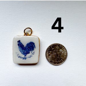 May include: A square white ceramic pendant featuring a blue rooster illustration and a gold-toned metal jump ring. The pendant is positioned next to a United States one dime coin for scale, with the number 4 printed in black in the upper right.