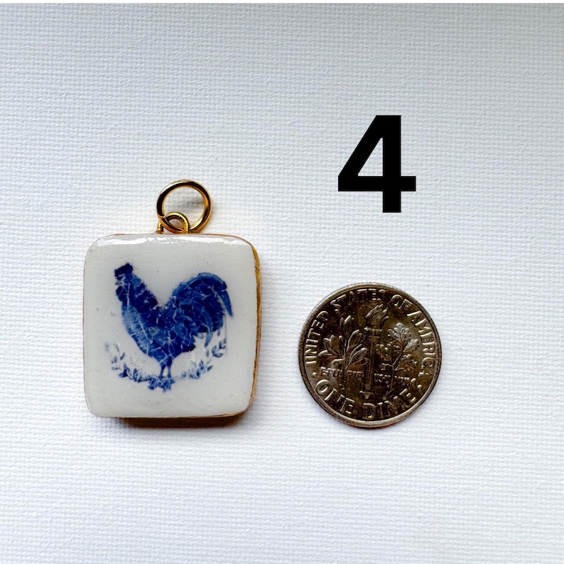May include: A square white ceramic pendant featuring a blue rooster illustration and a gold-toned metal jump ring. The pendant is positioned next to a United States one dime coin for scale, with the number 4 printed in black in the upper right.