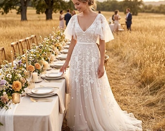 May include: A floor-length white dress featuring a V-neckline, flutter sleeves, and a sheer overlay adorned with intricate white floral embroidery. The garment has a fitted bodice and a flowing skirt that extends to the ground in a soft, layered silhouette.