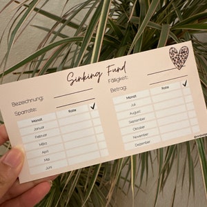 May include: A light brown card with the text "Sinking Fund" in black cursive writing. The card has a table with columns for "Month", "Rate", and a checkmark. The card also has a section for "F&auml;lligkeit" and "Betrag".