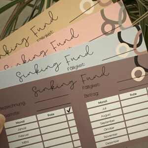 May include: A brown printable sinking fund tracker with a checklist and a table to track monthly payments. The table includes columns for month, rate, and amount. The text on the tracker says "Sinking Fund" and "F&auml;lligkeit".