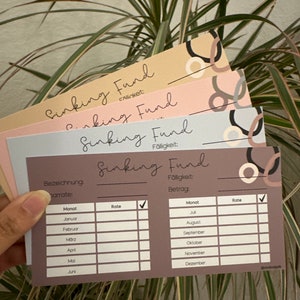 May include: A brown card with the text "Sinking Fund" and a table with columns for month, rate, and checkmark. The table is for tracking monthly savings for a sinking fund.