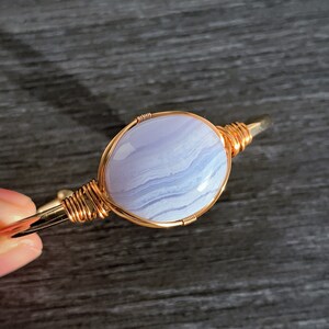 May include: A gold wire wrapped bracelet with a light blue agate stone. The stone has a swirling pattern of white and blue.