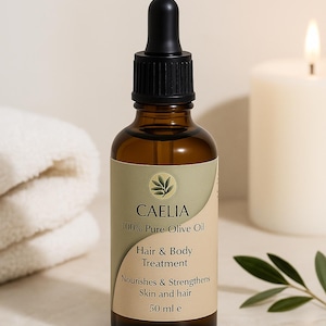 Può includere: Una bottiglia di vetro marrone di CAELIA 100% Olio d'Oliva Puro per il trattamento di capelli e corpo. L'etichetta indica che nutre e rinforza la pelle e i capelli. La bottiglia è da 50 ml. Una candela bianca e un asciugamano bianco piegato sono sullo sfondo.