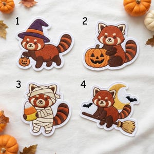May include: Four embroidered patches featuring red pandas in Halloween themes. Patch 1 shows a red panda in a purple witch hat holding a pumpkin bucket. Patch 2 shows a red panda sitting with a jack-o'-lantern. Patch 3 shows a mummy red panda holding candy corn. Patch 4 shows a red panda on a broomstick with a moon and bats.